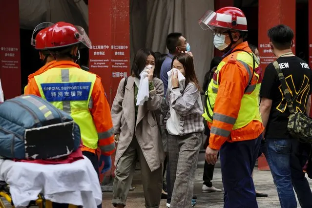 People walk out from the World Trade Centre where is located in the city's popular Causeway Bay shopping district of Hong Kong, Wednesday, December 15, 2021. Dozens of people are trapped on the rooftop of the Hong Kong skyscraper after a major fire broke out Wednesday, as firefighters rushed to rescue them and put out the blaze. (Photo by Kin Cheung/AP Photo)
