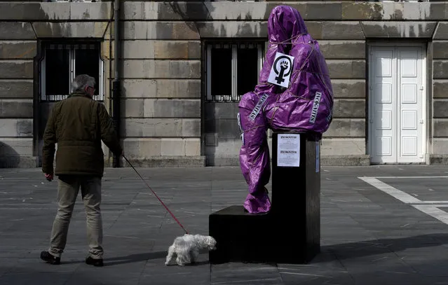 A man and his dog walk past the sculpture of a woman covered in paper and ropes as part of a performance to protest the lack of visibility of women in public spaces, on International Women's Day in Oviedo, Spain, March 8, 2017. The covered statue is La Pensadora (The female Thinker) by Spanish artist Jose Luis Fernandez. (Photo by Eloy Alonso/Reuters)