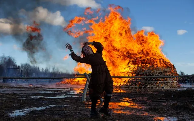 In this photo taken on Saturday, March 9, 2019, a visitor dances in front of a sculpture burning at the Maslenitsa (Shrovetide) festival at the Nikola-Lenivets art park in Nikola-Lenivets village, about 200 kilometers (125 miles) south-west of Moscow, Russia. As part of the celebrations of Maslenitsa (Shrovetide) Holiday in Russian, a folk holiday which heralds the beginning of spring, contemporary artist and park founder Nikolay Polissky built a giant sculpture made of wood and hay which was burnt to ashes during a traditional bonfire. (Photo by Alexander Zemlianichenko Jr./AP Photo)
