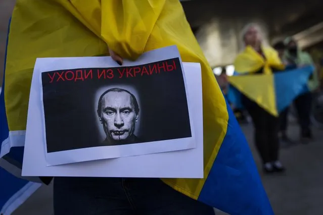 A demonstrator holds a banner depicting Russian President Vladimir Putin during a pro-Ukraine protest outside the Russian Embassy, after Russian troops have launched their anticipated attack on Ukraine, in Tel Aviv, Israel, Thursday, February 24, 2022. Sign in Russian reads “get out of Ukraine”. (Photo by Oded Balilty/AP Photo)