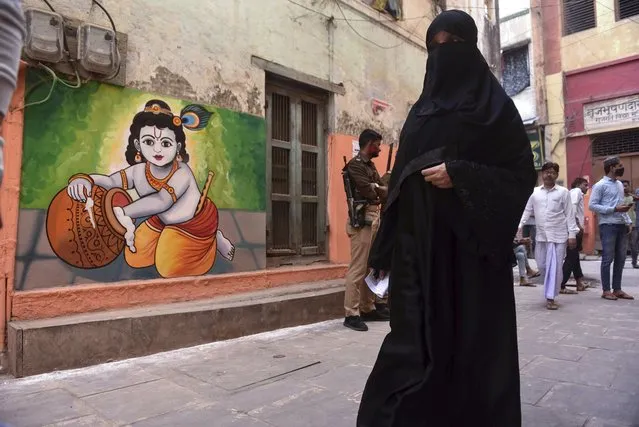 A burqa clad Muslim woman walks past a wall painting of Hindu god Krishna as she arrives to cast her vote during the seventh and final phase of Uttar Pradesh state legislature elections in Varanasi district, Uttar Pradesh, India, Monday, March 7, 2022. (Photo by Amar Deep Sharma/AP Photo)