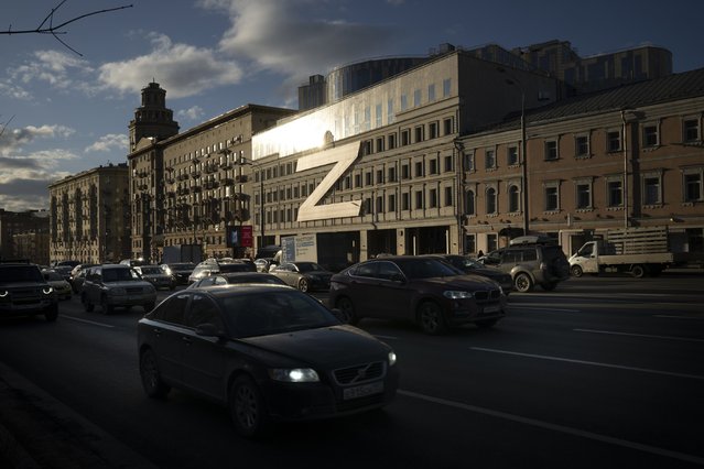 Cars drive a street with a huge letter Z, which has become a symbol of the Russian military, and a hashtag reading “We don't abandon our own” on a building during sunset in Moscow, Russia, Wednesday, March 30, 2022. (Photo by AP Photo/Stringer)