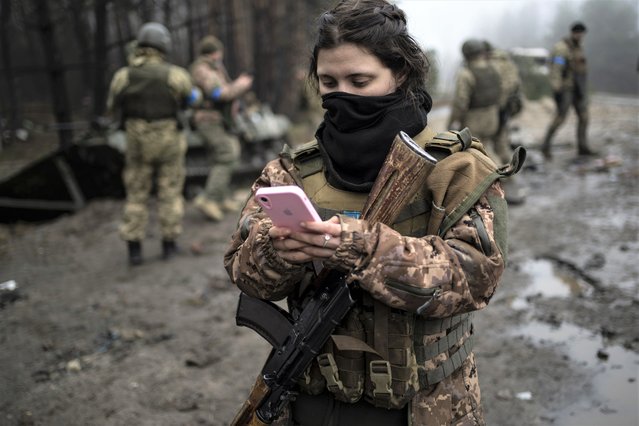 Ukrainian army soldier Dasha, 22, checks her phone after a military sweep to search for possible remnants of Russian troops after their withdrawal from villages in the outskirts of Kyiv, Ukraine, Friday, April 1, 2022. (Photo by Rodrigo Abd/AP Photo)