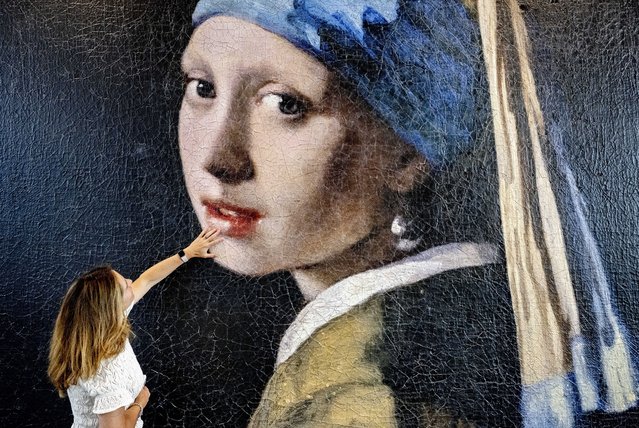 A woman touches the surface of an enlarged version of the famous painting “Girl with a Pearl Earring” by Johannes Vermeer at the “Mauritshuis” museum in The Hague, The Netherlands, 08 June 2023. The Vermeer painting has been enlarged a 100-times as a 3D print to become a four-meters high plastic colossus which is exhibited in the foyer of the museum. The giant 3D print clearly shows how the canvas has developed over the years and which painting techniques have been used. (Photo by Robin Utrecht/EPA)