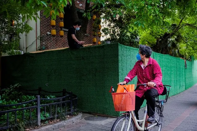 A woman passes a resident sitting on a barrier as she rides a bicycle at a closed residential area during lockdown, amid the coronavirus disease (COVID-19) outbreak, in Shanghai, China, May 30, 2022. (Photo by Aly Song/Reuters)