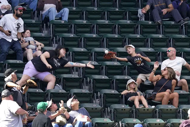 Baseball fans reach for a foul ball by Los Angeles Dodgers' Max Muncy in the upper deck of U.S. Cellular Field during the sixth inning of a baseball game between the Chicago White Sox and the Dodgers Thursday, June 9, 2022, in Chicago. (Photo by Charles Rex Arbogast/AP Photo)