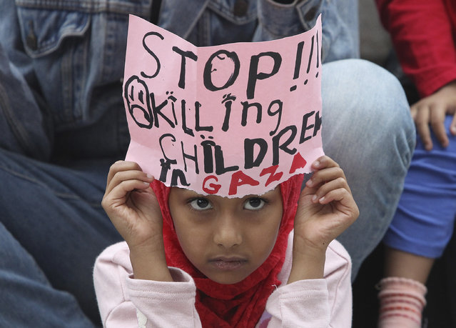 A Palestinian girl holding a sheet of paper written with a slogan attends a rally against the Israeli military operations in Gaza and the West Bank near the Israeli Embassy in Seoul, South Korea, Saturday, July 26, 2014. Israel and Hamas began a 12-hour humanitarian cease-fire in Gaza Saturday after the efforts of U.S. Secretary of State John Kerry failed to produce a longer truce aimed at ending nearly three weeks of fighting. (Photo by Ahn Young-joon/AP Photo)