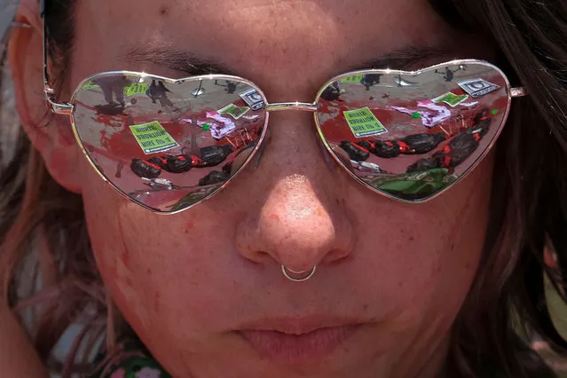 Body bags and coat hangers, laying in a pool of fake blood, are reflected in the heart-shaped glasses of an abortion rights activist during a “die-in” protest at the Urban Light sculpture, outside the Los Angeles County Museum of Art on July 28, 2022, in Los Angeles, to call on the federal government to restore abortion rights nationwide. (Photo by Ringo Chiu/AFP Photo)