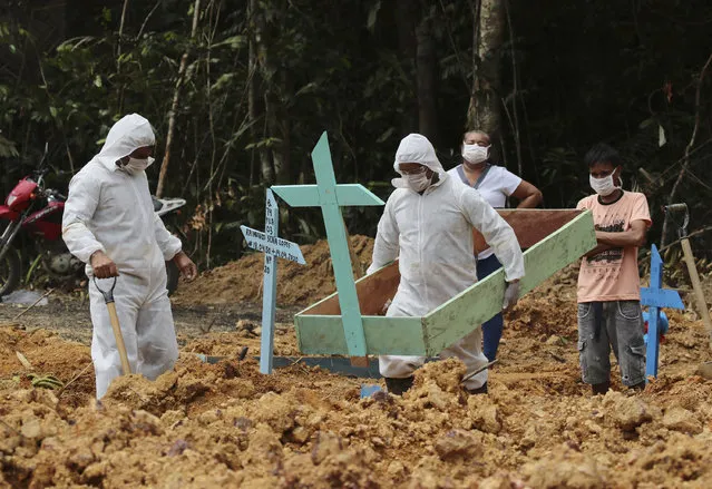 In this April 16, 2020 photo, funeral workers in protective gear prepare the grave of a woman who is suspected to have died of COVID-19 disease, at the Nossa Senhora Aparecida cemetery, in Manaus, Amazonas state, Brazil. Gravediggers buried 60 people that day, about triple the pre-virus average, according to a cemetery official. (Photo by Edmar Barros/AP Photo)