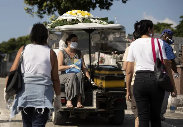 A woman wearing a face mask sits next the coffin of a relative as she's transported by a cemetery worker to the burial site at the Nossa Senhora das Gracas cemetery in Duque de Caxias, Rio de Janeiro, Brazil, Monday, April 27, 2020. The deceased person was previously held in a refrigerator for confirmed and suspected victims of of COVID-19, according to the administration of the cemetery. (Photo by Silvia Izquierdo/AP Photo)
