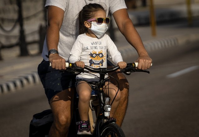 A girl wearing a protective face mask as a preventive measure against the spread of the new coronavirus ride a bicycle with her father in Havana, Cuba, Saturday, March 21, 2020. (Photo by Ramon Espinosa/AP Photo)