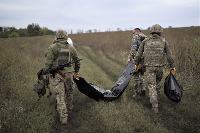 Ukrainian servicemen carry a bag containing the body of a Ukrainian soldier, center, as one of them, right, carries the remains of a body of a Russian soldier in a retaken area near the border with Russia in Kharkiv region, Ukraine, Saturday, September 17, 2022. (Photo by Leo Correa/AP Photo)
