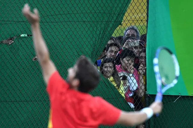 People peer into the tennis court where Spain's Rafael Nadal and Spain's Marc Lopez are playing against Canada's Vasek Pospisil and Canada's Daniel Nestor during their men's doubles semi-final tennis match at the Olympic Tennis Centre of the Rio 2016 Olympic Games in Rio de Janeiro on August 11, 2016. (Photo by Luis Acosta/AFP Photo)
