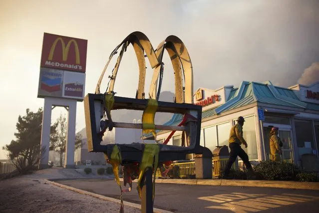 A melted sign from a McDonald's restaurant shows the damage as firefighters check the area after a wildfire swept through Cajon Junction, California, USA, 16 August 2016. According to reports, the fast-moving Blue Cut Fire, which consumed so far some 6,500 acres with a zero percent containment, prompted the mandatory evacuation of the whole community of Wrightwood. (Photo by Eugene Garcia/EPA)
