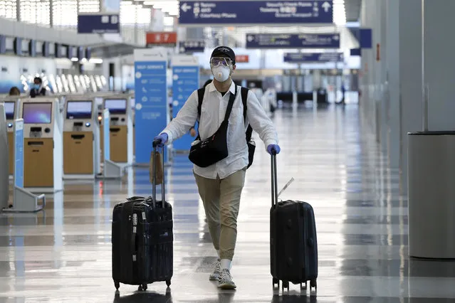 A traveler wears a mask and protective goggles as he walks through Terminal 3 at O'Hare International Airport Tuesday, June 16, 2020, in Chicago. Beginning June 16 at American Airlines and June 18 at United Airlines, all passengers and crew members will be required to wear masks to prevent the spread of COVID-19 pandemic. (Photo by Nam Y. Huh/AP Photo)
