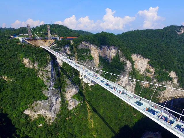Visitors walk across a glass-floor suspension bridge in Zhangjiajie in southern China's Hunan Province Saturday, August 20, 2016. (Photo by Chinatopix via AP Photo)