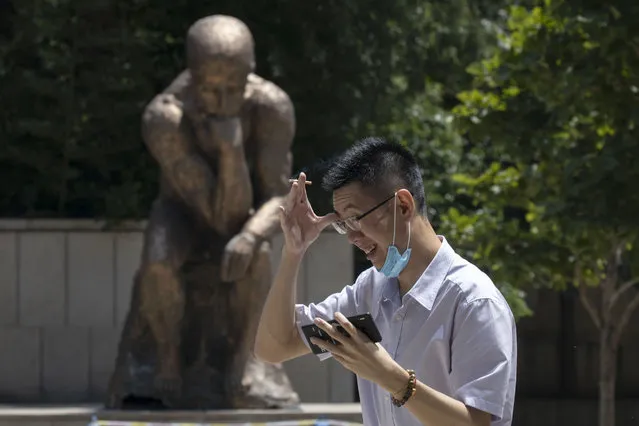 A man lowers his mask to smoke as he passes by a statue in the likeness of The Thinker in Beijing, China on Monday, July 6, 2020. (Photo by Ng Han Guan/AP Photo)