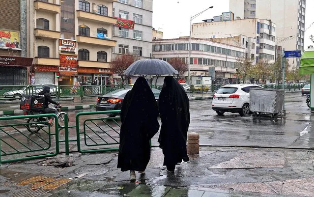 Women share an umbrella as they stand at Enghelab Square in Iran's capital Tehran on December 5, 2022. (Photo by Atta Kenare/AFP Photo)