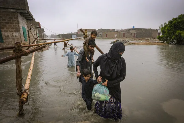A family wade through a flooded area during a heavy monsoon rain in Yar Mohammad village near Karachi, Pakistan, Thursday, August 27, 2020. Pakistan's military said it will deploy rescue helicopters to Karachi to transport some 200 families to safety after canal waters flooded the city amid monsoon rains. (Photo by Fareed Khan/AP Photo)