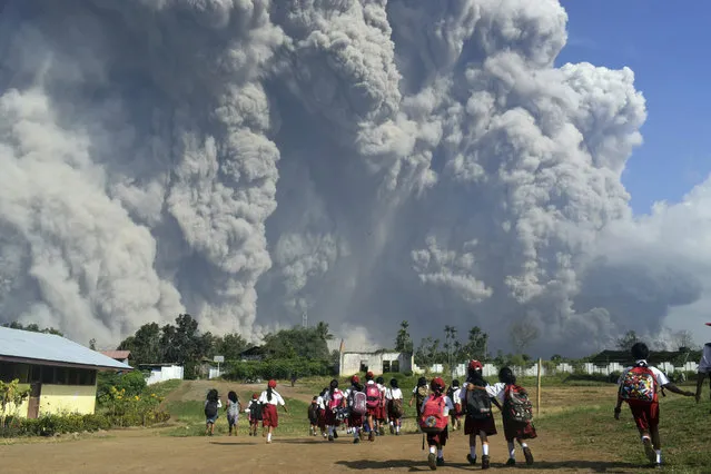 School children walk as Mount Sinabung erupts in Karo, North Sumatra, Indonesia, Monday, February 19, 2018. Rumbling Mount Sinabung on the Indonesian island of Sumatra has shot billowing columns of ash more than 5,000 meters (16,400 feet) into the atmosphere and hot clouds down its slopes.  The volcano, one of three currently erupting in Indonesia, was dormant for four centuries before exploding in 2010. (Photo by AP Photo/Sarianto)