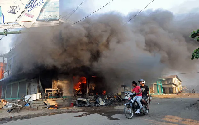 Residents ride a motorcycle past a burning building in riot-hit Meiktila, central Myanmar on March 22, 2013. Charred bodies lay unclaimed on the streets of a riot-hit town in central Myanmar, witnesses said, as global pressure mounted for an end to the Buddhist-Muslim unrest. Parts of Meiktila have been reduced to ashes in the most serious communal violence to hit the former junta-ruled nation since last year, leaving the authorities struggling to bring the situation under control. (Photo by Soe Than Win/AFP Photo)