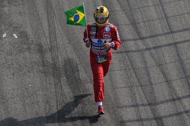 A man runs holding a Brazilian national flag as he takes part in the Ayrton Senna Racing Day at the Jose Carlos Pace racetrack, also known as Interlagos, in Sao Paulo, Brazil, on May 1, 2024, during the 30th anniversary of his death. Thirty years after his death at the San Marino Grand Prix, Ayrton Senna is still adored in Formula One, a sport his fatal accident reshaped. The 34-year-old Brazilian was leading at Imola on May 1, 1994, when he went off the track at the Tamburello curve and smashed into a concrete wall. (Photo by Nelson Almeida/AFP Photo)