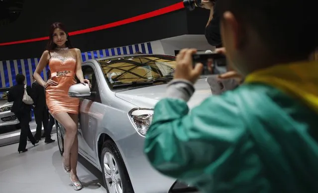 A child takes a picture of a model as she poses next to a car during the the 15th Shanghai International Automobile Industry Exhibition in Shanghai, in this April 21, 2013 file photo. Female models in tight dresses and miniskirts may be banned from one of Asia's premier car exhibitions in Shanghai in 2015. (Photo by Carlos Barria/Reuters)