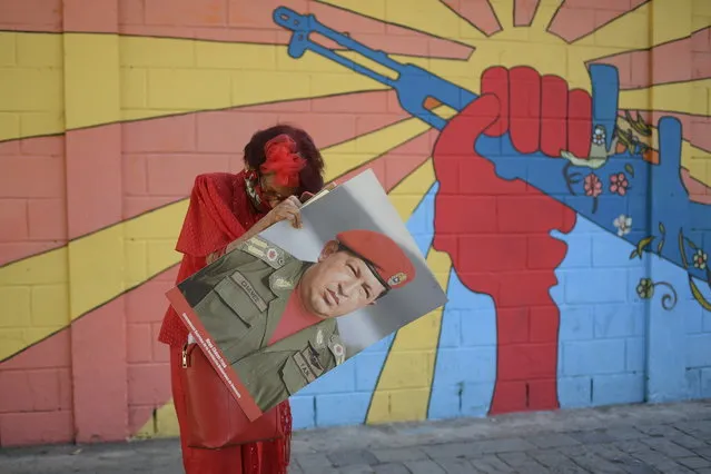 A government supporter known as “Caperucita”, or Little Red Riding Hood, holds a photo of late Venezuelan President Hugo Chavez as she looks for something in her purse in Plaza Bolivar, near the National Assembly where newly elected National Assembly lawmakers will be sworn-in and hold their first session of the year in Caracas, Venezuela, Tuesday, January 5, 2021. (Photo by Matias Delacroix/AP Photo)