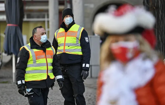 A carnival reveler is watched by public order guards at the “Alter Markt” where normally tens of thousands of revelers dressed in carnival costumes would celebrate the start of the street carnival in Cologne, Germany, Thursday, February 11, 2021. This year all carnival celebrations are banned due to the coronavirus pandemic. (Photo by Martin Meissner/AP Photo)
