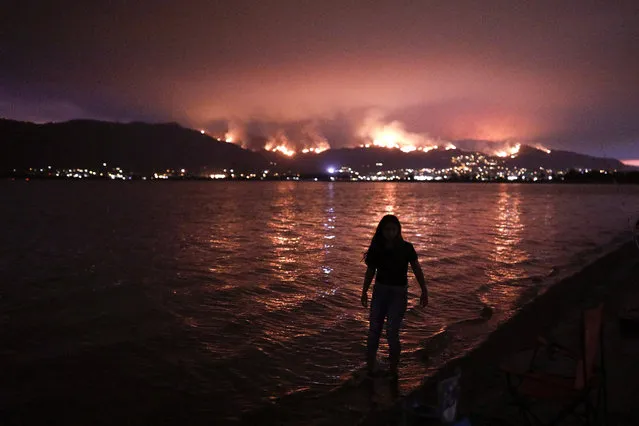 A girl wades through water while watching a wildfire burn in the Cleveland National Forest in Lake Elsinore, Calif., Wednesday, August 8, 2018. Evacuations have been ordered for several small mountain communities near where a forest fire continues to grow in Southern California. (Photo by Jae C. Hong/AP Photo)