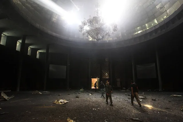 Anti-Gaddafi fighters walk inside a hall of the Ouagadougou conference center which was destroyed by heavy artillery fire as they take control of the building known for hosting regional meetings for Arab and African leaders in Sirte, Libya October 9, 2011. A timeline of images dating from 2010 from Sirte, Libya, the home town of deposed Libyan leader Muammar Gaddafi. Libyan forces battling Islamic State in the city of Sirte say they have defeated the militant group after months of street to street fighting backed by U.S. air strikes. Islamic State took control of the city more than a year ago and set up its main base outside Syria and Iraq. (Photo by Asmaa Waguih/Reuters)