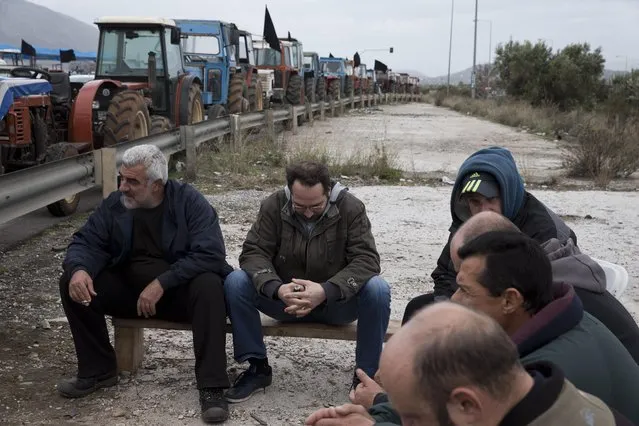Farmers sit in front of their parked tractors as they blockade a road that links the international airport with the southern and eastern suburbs of the Greek capital, in Koropi, near Athens, Friday, February 12, 2016. Farmers from across Greece have begun gathering in Athens for a two-day protest against the government and its plans to impose new tax hikes and pension charges demanded by the bailout lenders. (Photo by Petros Giannakouris/AP Photo)