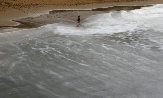 A woman stands on a sandy beach as waves swirl around Ghajn Tuffieha (Apple's Eye) Bay on the northwest coast of Malta, February 18, 2016. (Photo by Darrin Zammit Lupi/Reuters)