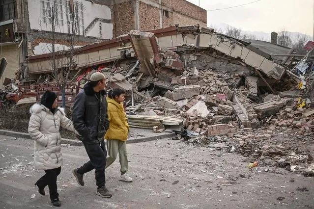 People walk past a collapsed building after an earthquake in Dahejia, Jishishan County in northwest China's Gansu province on December 19, 2023. (Photo by Pedro Pardo/AFP Photo)