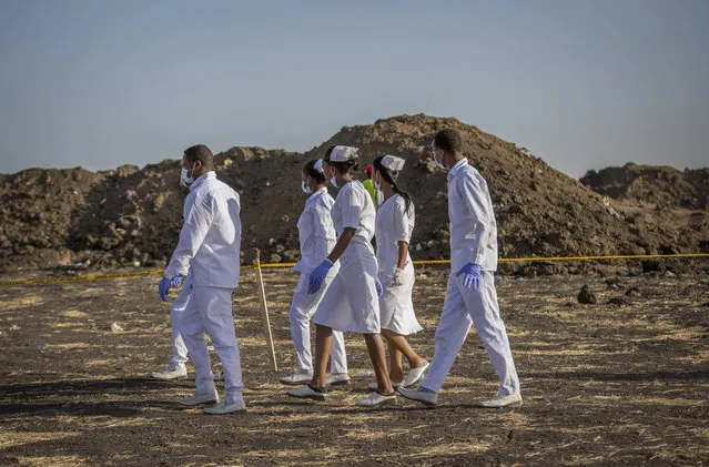 Nurses walk to collect materials, under the instruction of investigators, at the scene where the Ethiopian Airlines Boeing 737 Max 8 crashed shortly after takeoff on Sunday killing all 157 on board, near Bishoftu, or Debre Zeit, south of Addis Ababa, in Ethiopia Tuesday, March 12, 2019. (Photo by Mulugeta Ayene/AP Photo)