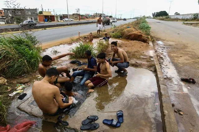 People wash themselves along a road at an area that is flooded due to a broken pipe in San Felix, Venezuela on March 12, 2019. (Photo by William Urdaneta/Reuters)