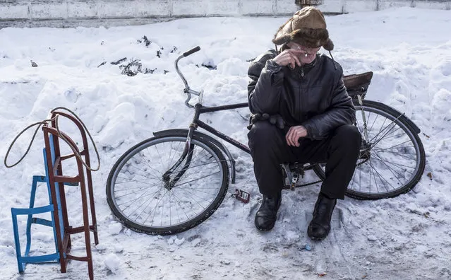 A man smokes sitting on a bicycle as he waits to receive humanitarian aid at the humanitarian aid center in Avdiivka, eastern Ukraine, Friday, February 3, 2017. Strong shelling hit both government- and rebel-controlled areas of eastern Ukraine in a continued escalation of the country's fighting. (Photo by Evgeniy Maloletka/AP Photo)