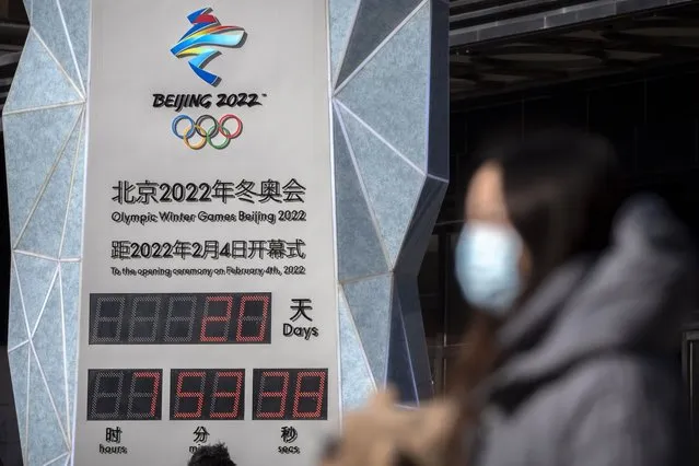 A woman wearing a face mask to protect against COVID-19 walks past a clock counting down the time until the opening ceremony of the 2022 Winter Olympics in Beijing, Saturday, January 15, 2022. Beijing has reported its first local omicron infection, according to state media, weeks before the Olympic Winter Games is due to start. (Photo by Mark Schiefelbein/AP Photo)
