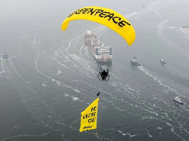 A paraglider of Greenpeace flying above the Russian oil tanker Michail Ulyanov with a banner with the words “No Arctic Oil!” near the harbour of Rotterdam, 1 May 2014. The environmental organisation is demonstrating against the ship carrying the first oil from the Arctic Sea to Rotterdam. (Photo by Ruben Neugebauer/Getty Images)