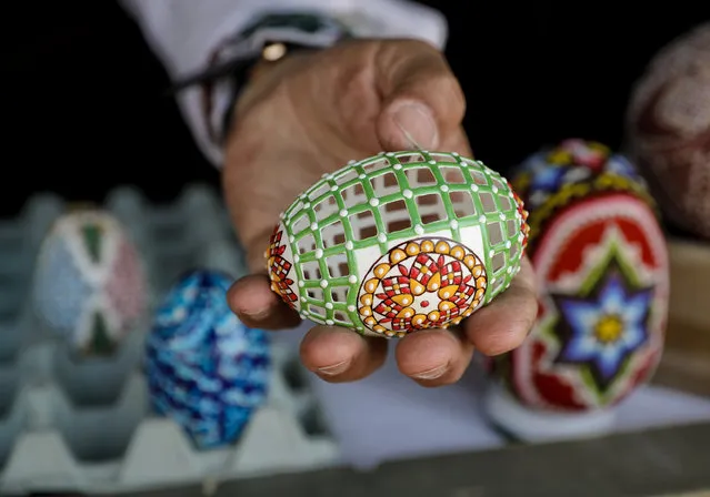 In this Thursday, April 13, 2017, picture artisan Nicu Poenariu displays for a photograph an Easter egg on sale at a fair in Bucharest, Romania. New trends are joining old traditions in Romania this Easter. In the predominantly Christian Orthodox country of 19 million, age-old crafts such as intricate egg decorating and painted religious icons are a major feature of the Holy Week run-up to Easter Sunday. But a more commercial flavor has slowly crept into the celebrations. At an Easter fair outside the Bucharest palace built by the late Communist leader Nicolae Ceausescu, entertainers strutted around wearing giant rabbit heads. Huge models of colored eggs in baskets dotted the displays. An oversized hen pulled a cart while a plastic rabbit sat in the back with a model of large painted egg, scenes that could have been inspired by “Alice in Wonderland”. Painted religious symbols, a major feature of Christian Orthodox observances, also were on display and for sale at the fair and the patriarchy, the seat of the Romanian Orthodox Church. Tradition flourished elsewhere in the Romanian capital. Craftsmen such as Nicu Poenaru skillfully embellished hen, ostrich and goose eggs by hollowing out the contents and carefully piercing tiny holes in the shells, creating objects of artistic and religious value. Prices range from 15 lei to 150 lei ($3.50 to $35) depending on the size and intricacy of the design. While humans in rabbit costumes were all the rage at the fair, one child got to see a real rabbit close up, crouching down by the animal's cage with wonder. (Photo by Vadim Ghirda/AP Photo)