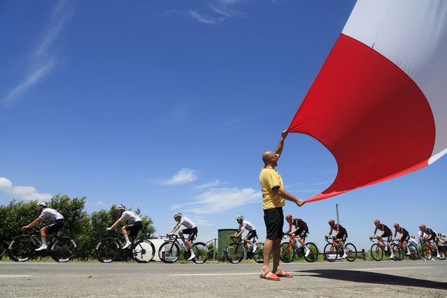 A spectator waves a flag as riders of UAE Team Emirates (L) and INEOS Grenadiers (R) pass in front of him during the second stage of the 2024 Tour de France cycling race over 199km from Cesenatico to Bologna, Italy, 30 June 2024. (Photo by Guillaume Horcajuelo/EPA)