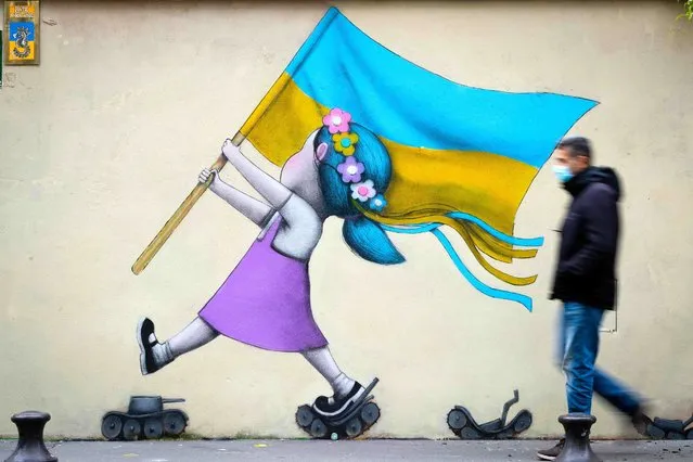 A bystander walks past a fresco by street artist Seth depicting a girl with a Ukrainian flag walking on tanks in Paris on March 01, 2022. (Photo by Joel Saget/AFP Photo)