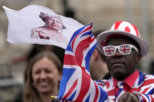 A Royal fan waves a flag showing Britain's Queen Elizabeth II as crowds gather ahead of a Service of Thanksgiving for the life of Prince Philip, Duke of Edinburgh at Westminster Abbey in London, Tuesday, March 29, 2022. (Photo by Frank Augstein/AP Photo)
