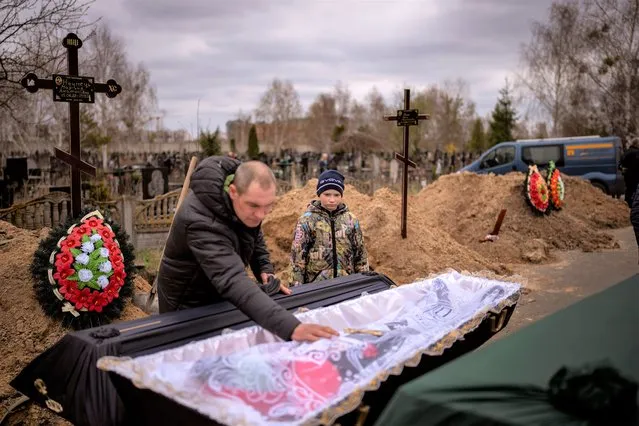 Vova, 10, looks at the body of his mother, Maryna, lying in a coffin as his father, Ivan Drahun, prays during her funeral in Bucha, on the outskirts of Kyiv, Ukraine, on Wednesday, April 20, 2022. Vova's mother died while they sheltered in a cold basement for more than a month during the Russian military's occupation. (Photo by Emilio Morenatti/AP Photo)