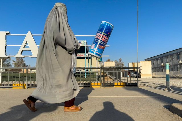 In this photo taken on August 29, 2024, an Afghan burqa-clad woman walks past an energy drink advertisement at Kandahar airport in Kandahar. The Taliban government has purged many signs of Western influence but a stimulant drink craze that arrived with US soldiers remains, and has even sprouted a thriving domestic industry. Alcohol is outlawed in Afghanistan but caffeine-rich energy drinks are guzzled by secret police, fed by mothers to suckling children and advertised on billboards more than even Taliban state propaganda. (Photo by Wakil Kohsar/AFP Photo)