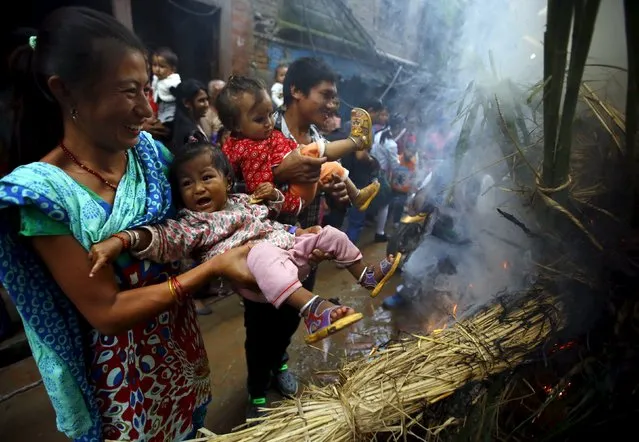 A woman swings a child around the fire, where an effigy of the demon Ghantakarna was burnt to symbolize the destruction of evil, during the Ghantakarna festival at the ancient city of Bhaktapur, Nepal August 12, 2015. (Photo by Navesh Chitrakar/Reuters)