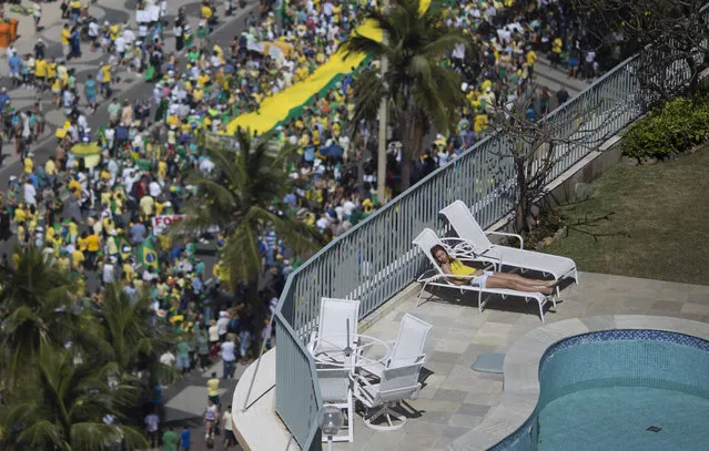 A woman sleeps in a residential penthouse while thousands below march in an anti-government protest demanding the impeachment of Brazil's President Dilma Rousseff, in at Copacabana beach, Rio de Janeiro, Brazil, Sunday, August 16, 2015. Demonstrators are taking to the streets across Brazil for a day of nationwide anti-government protests. President Rousseff's second term in office has been shaken by a snowballing corruption scandal involving politicians from her Workers  Party. (Photo by Leo Correa/AP Photo)