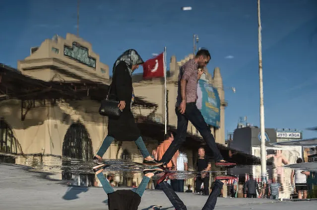 A reflection on waste liquid shows people walking in front of Haldun Taner Stage theatre on August 17, 2017, during a warm day at Kadiköy district in Istanbul. (Photo by  Ozan Kose/AFP Photo)