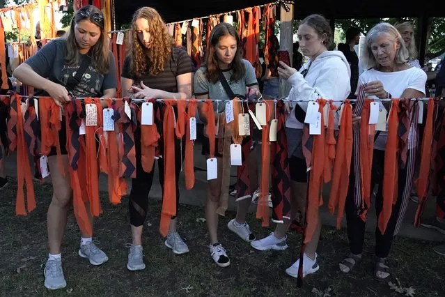 Residents from around the Highland Park, Ill., area tie up their hand written tags and orange ribbons during a vigil at Sunset Woods Park for the victims of Monday's Highland Park's Fourth of July parade, Thursday, July 7, 2022, in Highland Park, Ill. (Photo by Nam Y. Huh/AP Photo)