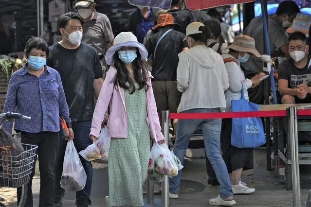 Residents wearing face masks carry their groceries as they leave an outdoor market in Beijing, Thursday, July 21, 2022. (Photo by Andy Wong/AP Photo)